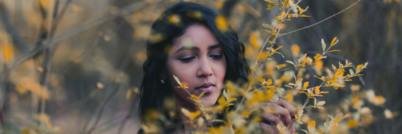 photo of woman standing behind autumn leaves with eyes closed or lowered