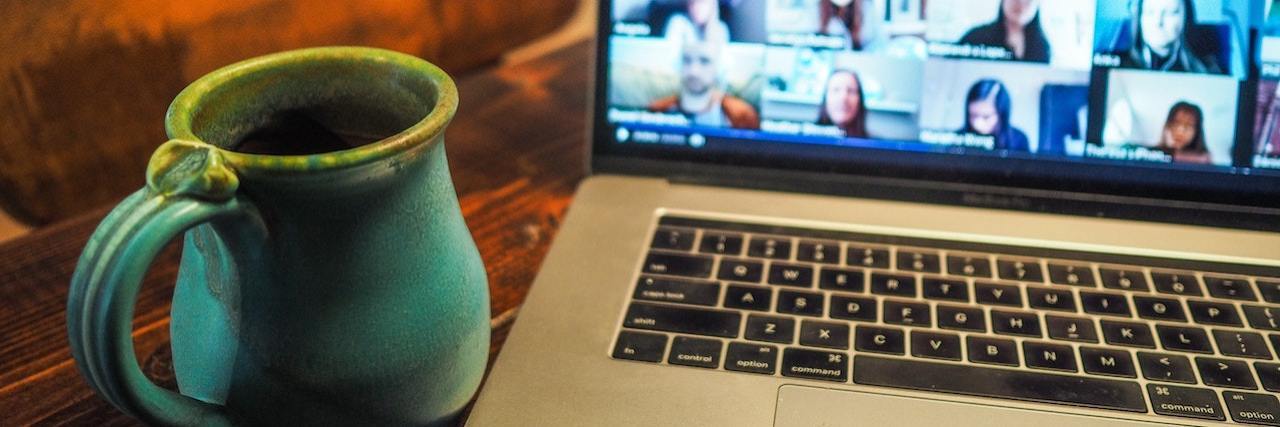 Work-From-Home Companies for People With a Disability Open laptop showing an in-progress Zoom meeting with a green clay coffee mug on a table next to the computer