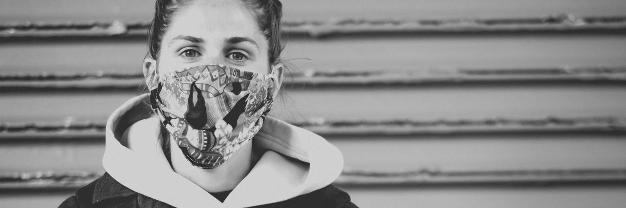 My OCD Was Surprisingly Calm During the COVID-19 Pandemic black and white photo of young woman wearing patterned face mask and standing against a shop shutter