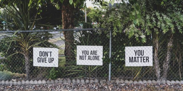 5 Reasons I'm Still Here After Experiencing Suicidal Thoughts Signs saying "Don't give up," "You are not alone" and "You Matter"