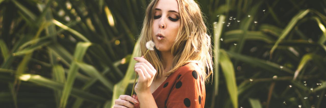 How To Cope With Overwhelming Emotions Without Thinking About Suicide photo of woman standing in front of large leaves, blowing dandelion seeds