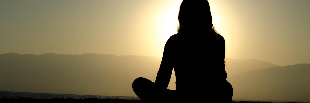 silhouette of woman sitting crosslegged in front of sun