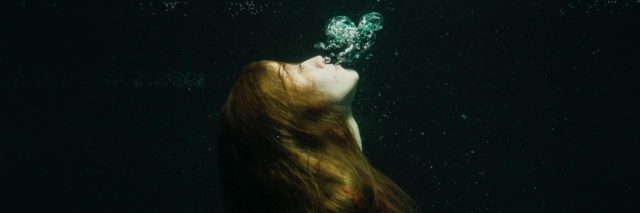 photo of woman in red dress underwater in darkness