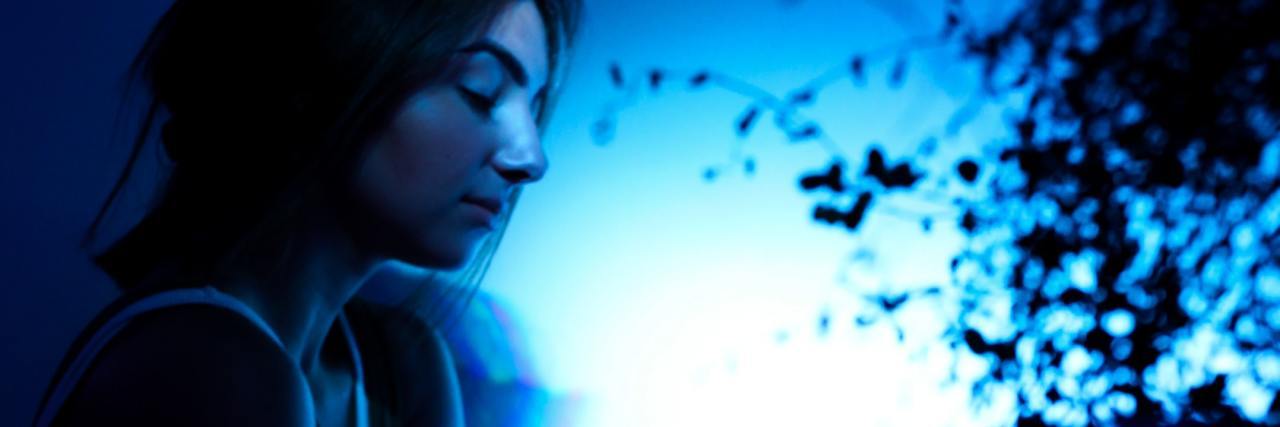 photo of unhappy woman in profile in blue light with leaves silhouetted