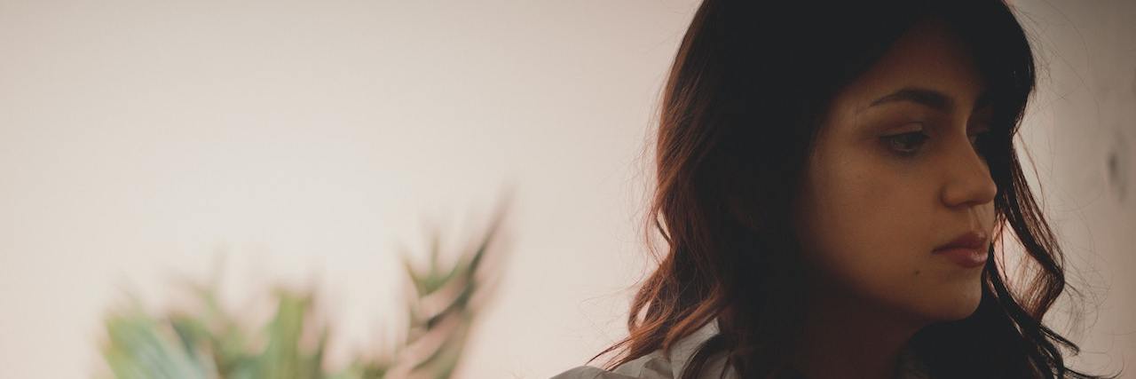 6 Things You Need to Know About Perinatal Mood Disorders Woman with long brown hair and bangs wearing a white button-up shirt looking off to the right