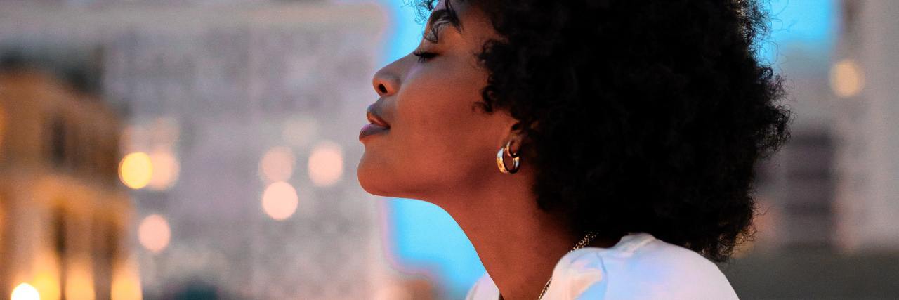 How I Still Have Hope in Life With Chronic Illness photo of Black woman standing on city roof with her eyes closed and head raised