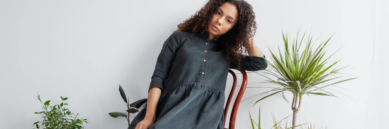 Growing up With Economic Privilege Didn't Stop My Mental Illness photo of woman sitting on a chair surrounded by plants and looking into camera