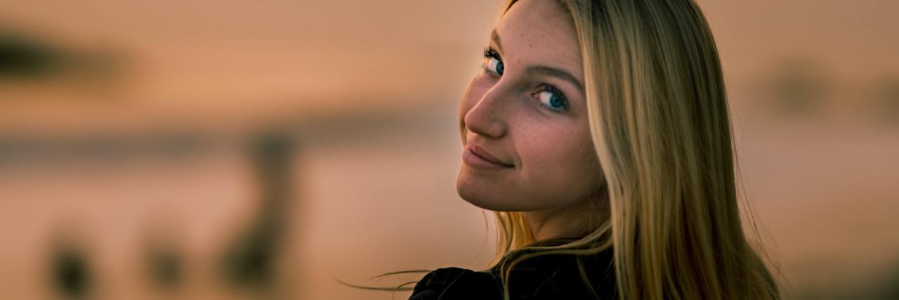 How To Track the Lies Anxiety Tells photo of young woman against unfocused background at sunset, looking back over shoulder and smiling