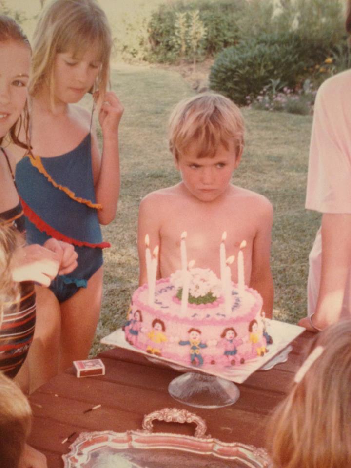 photo of the contributor as a child at a birthday party, looking unhappy in front of a pink cake