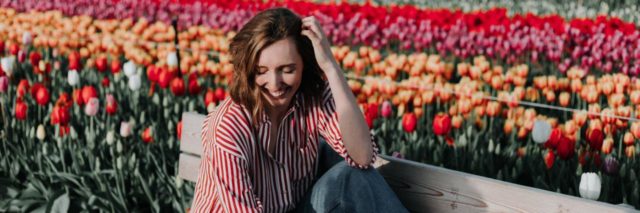 photo of smiling woman sitting on a bench beside a field of colourful flowers