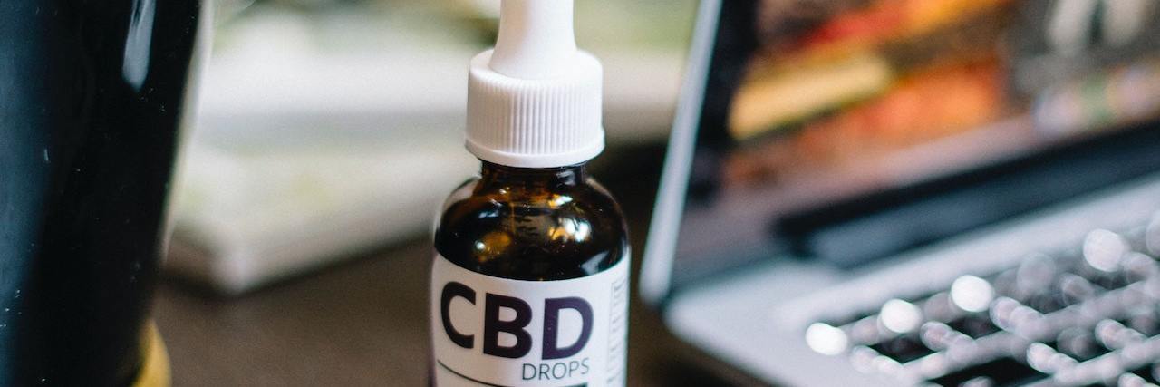 Bottle of CBD oil on a desk next to a potted plant and an open laptop