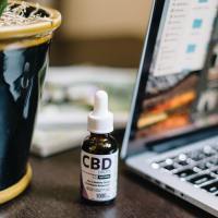 Bottle of CBD oil on a desk next to a potted plant and an open laptop