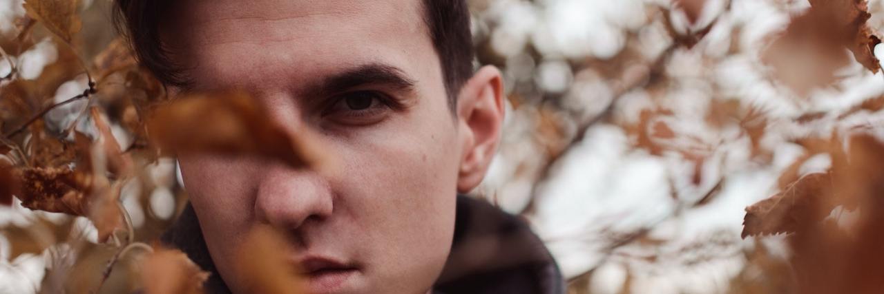 Better Supporting Loved Ones Struggling With Suicidal Thoughts Man peering through leaves on a tree
