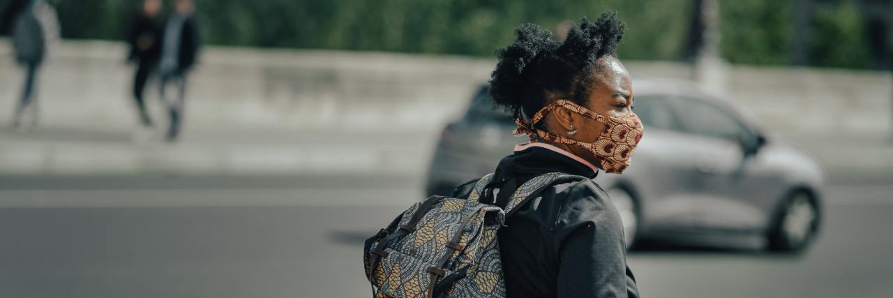 Black woman walking with a book bag and a mask on