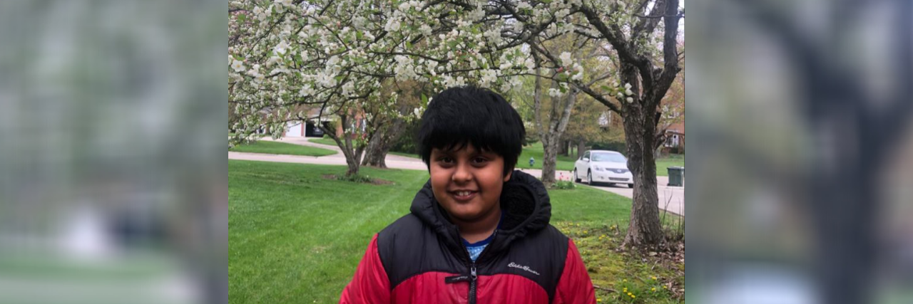 Tulika's son standing outside near a blossoming tree.