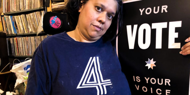 Priya sitting next to a sign that says "vote."