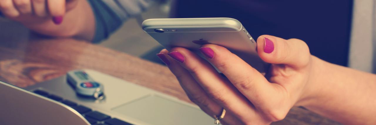 close up photo of a woman holding her smartphone in one hand while sitting near laptop