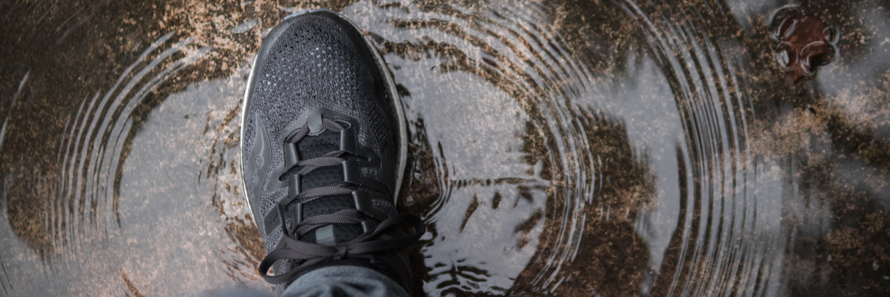 a dark tennis shoe walking though a puddle