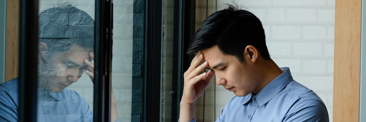 The Loneliness of Being Young With Tardive Dyskinesia Sad man standing by window.