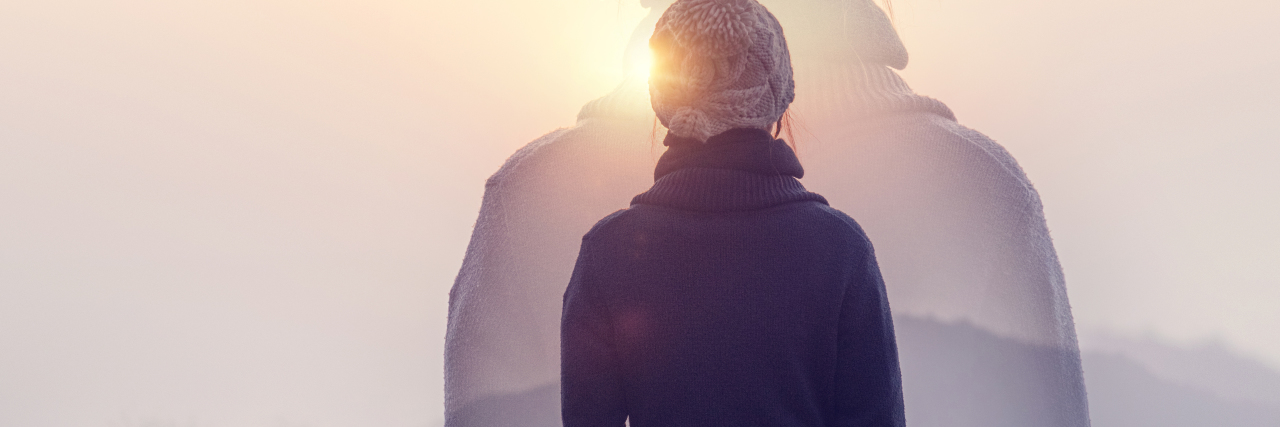 a woman staring at the mountains at sunrise with her hands in her coat pockets