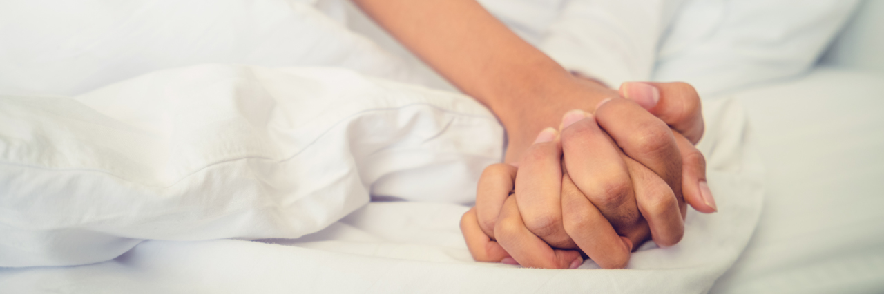 Hands of couple in bed.