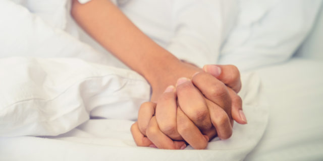 Hands of couple in bed.