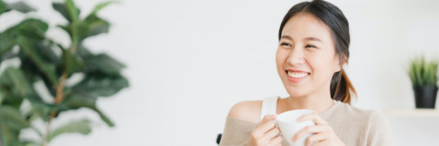 Asian woman smiling and holding a cup of coffee