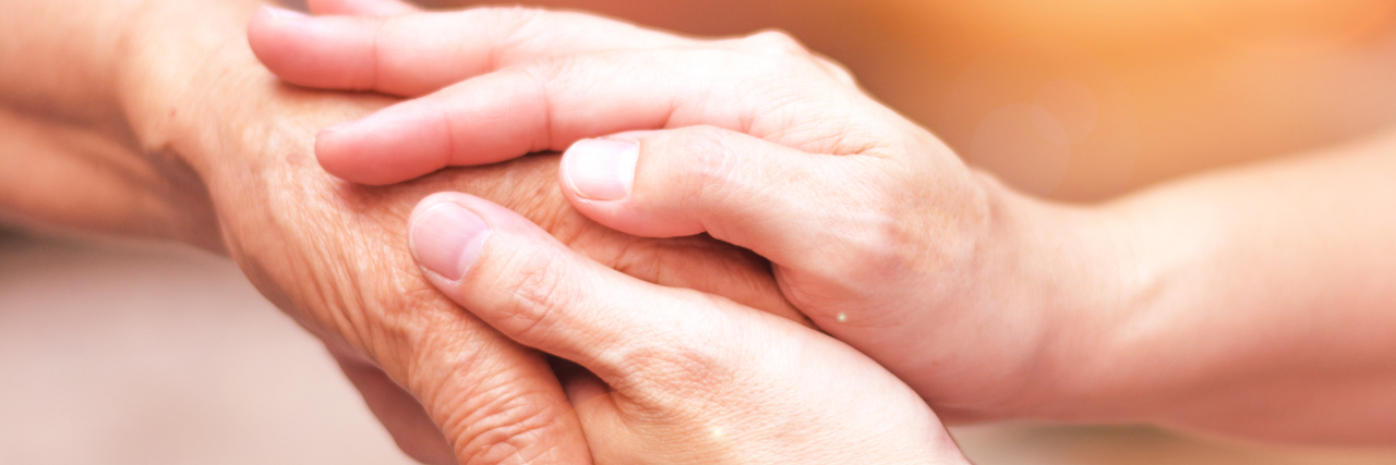 The Pain and Love of Caring for a Parent With Alzheimer’s Daughter's hand holding elderly mother's hand.