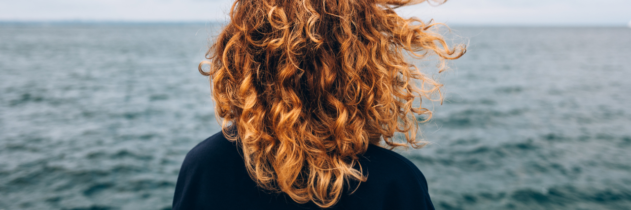 View from the back a woman with curly hair looks at the sea