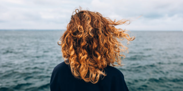 View from the back a woman with curly hair looks at the sea