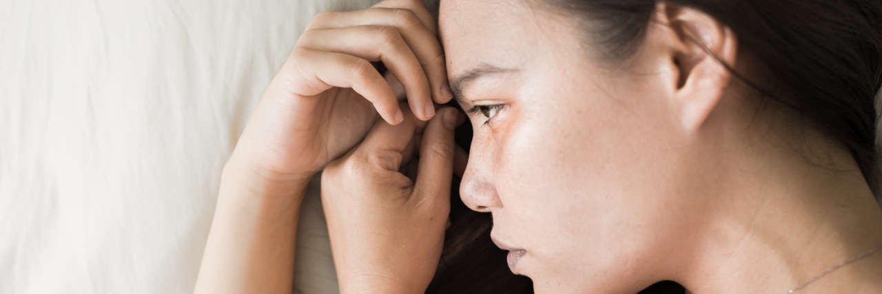 Deciding Whether to Have Kids With Multiple Autoimmune Syndrome close-up of a woman's face, feeling sad, lying on a pillow, with her hands near her face.