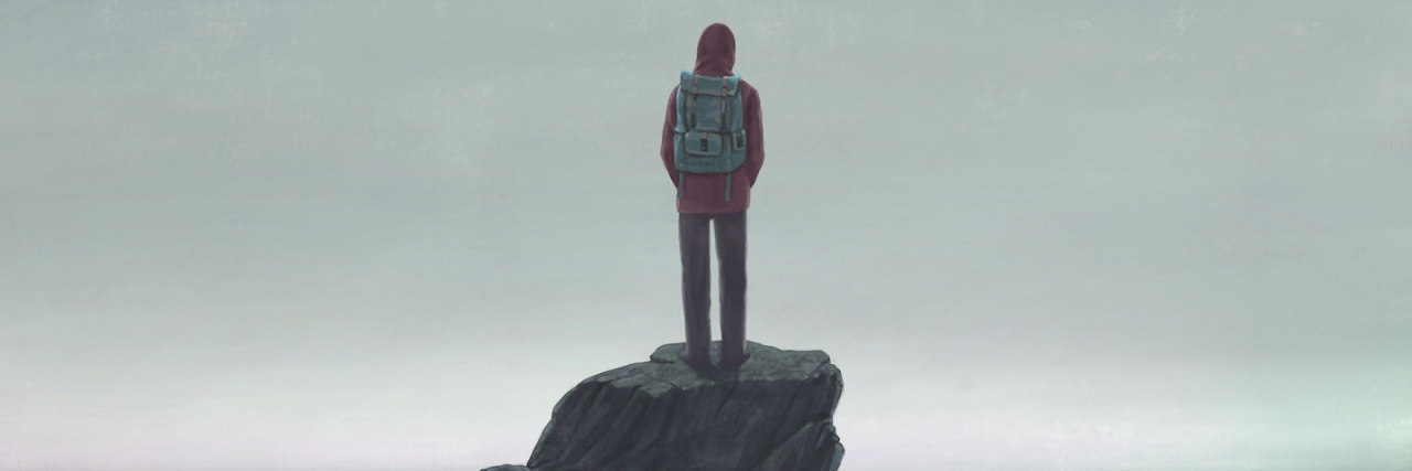 Man standing on a rock, looking out at the sea, wearing a backpack