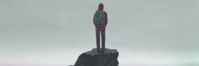 Man standing on a rock, looking out at the sea, wearing a backpack