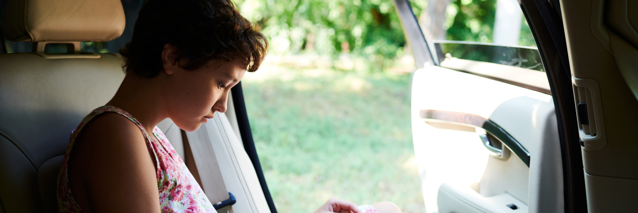 Why I Travel 600 Miles to Seek Help for Stiff Person Syndrome a teenage girl sitting in the back seat of a car reading a book