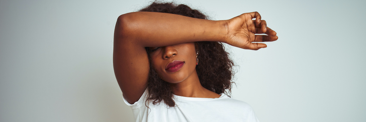 Young african american woman wearing t-shirt standing over isolated white background covering eyes with arm, looking serious and sad.