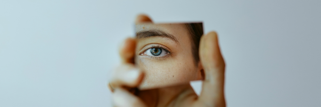 Mourning the Old Me After a Traumatic Brain Injury Hand holding mirror with reflection of eye.