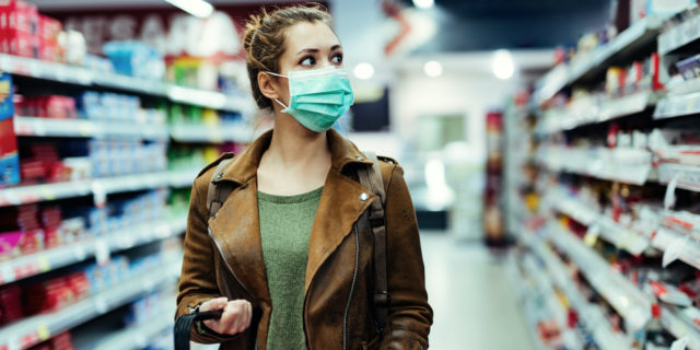 A young woman walking down the isle in a grocery stories with her mask on