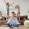 Woman meditating while her kids jump on the sofa.