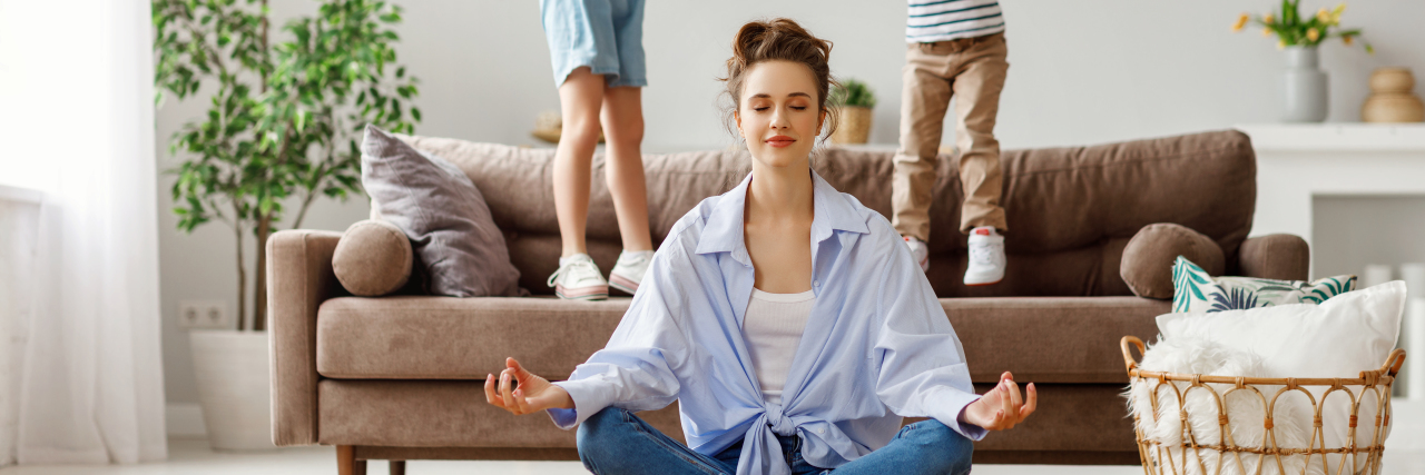 How Parents and Caregivers Can Combat Compassion Fatigue Parent sitting on the floor with eyes closed, practicing calm breathing as two energetic children jump on the couch behind her.