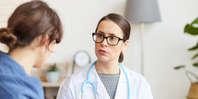 Young female doctor in white coat talking to her patient while visiting her