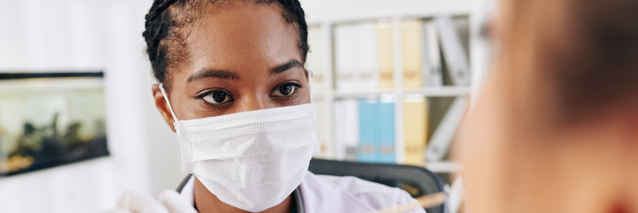 Black Doctors Work to Make Coronavirus Testing More Equitable Serious young Black general practitioner in medical mask asking patient to open mouth so she could check her throat