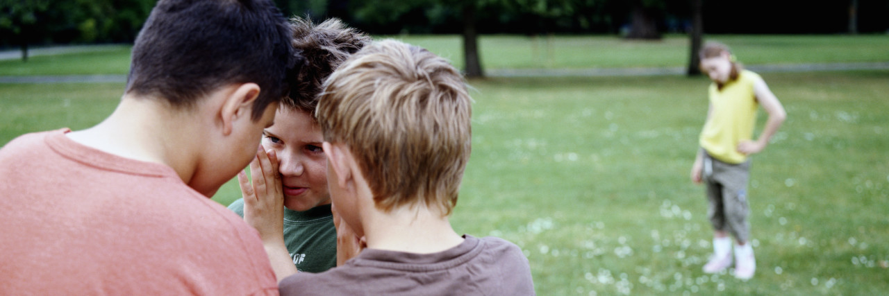 Why a Student With a Speech Disorder is Often the Target of Bullying a group of boys are in a park whispering and a girl is standing alone