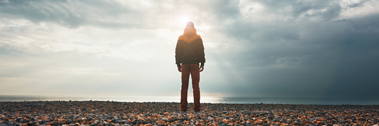 When Your Mental Illness Comes in Waves A man standing on a rocky beach, facing the water.