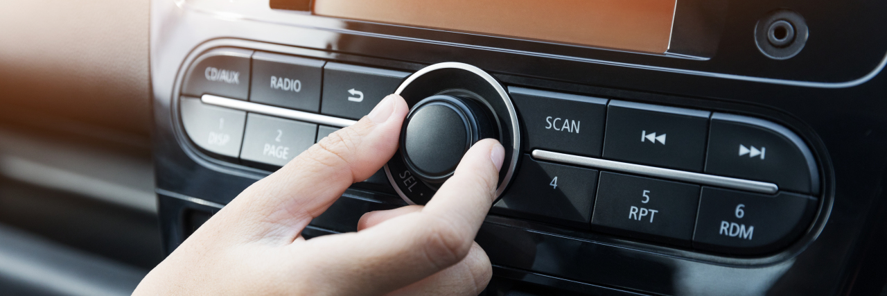 Woman turning button on car radio for listening to music.