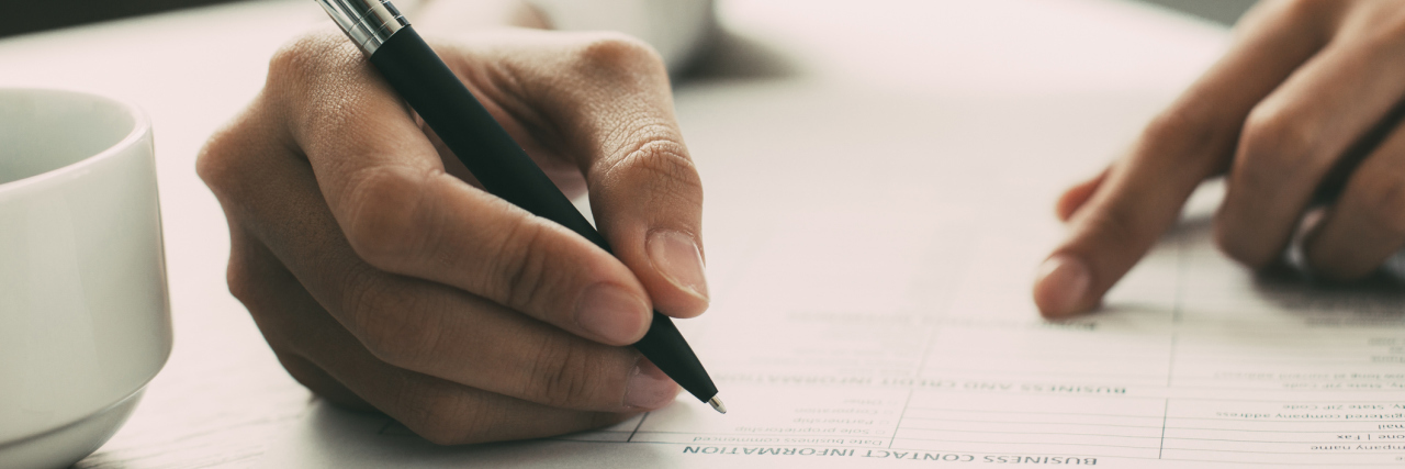 Applying for Disability Benefits Should Be Easier and Clearer hand holding a pen filling out an application