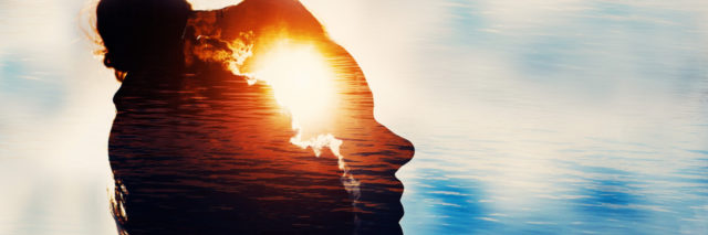 Silhouette of a woman's face looking at a blue sky with the sun in her head