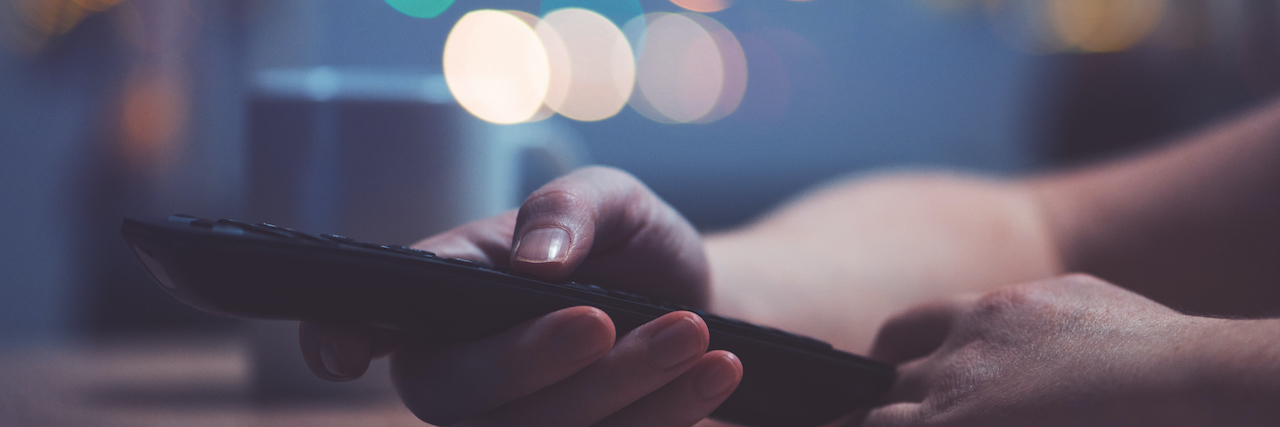 Watching TV Sitcoms Brought Me Relief From Stress and Anxiety Hand holding television remote control with blurry lights in background