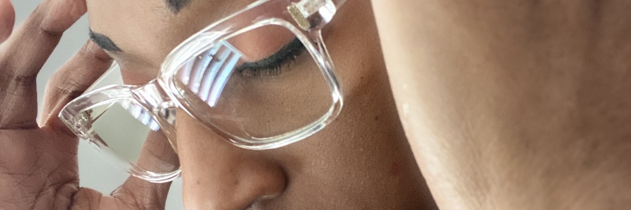 What It’s Like Being a Mom With Migraines a woman with glasses with her hands on her temples