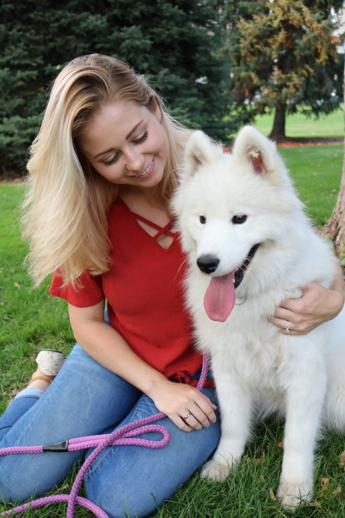 photo of woman sitting on the grass with a white furry dog