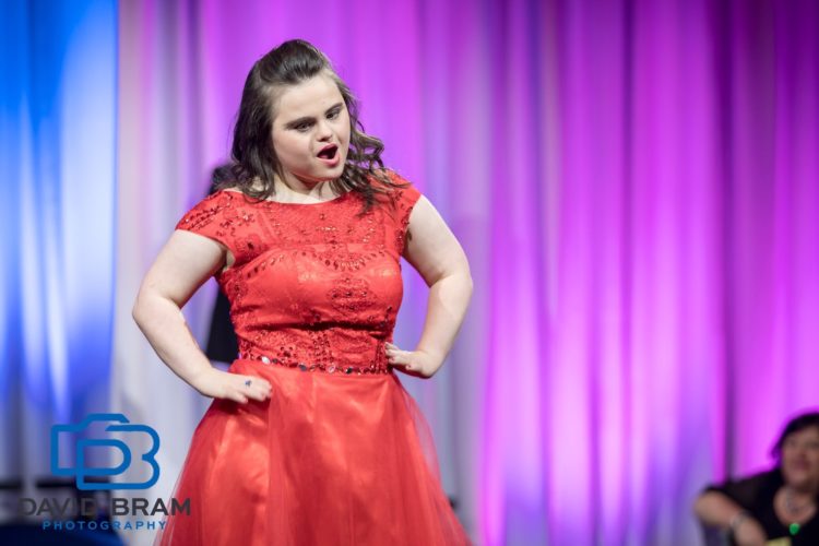 Rachel striking a pose on stage wearing a red dress.